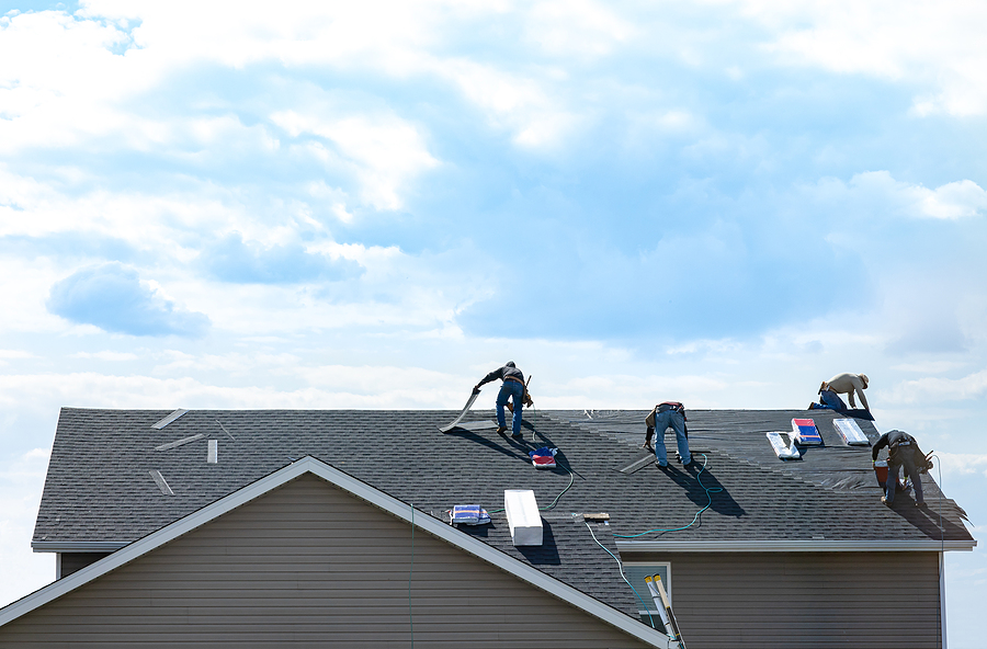 4 construction workers fixing roof against clouds blue sky, install shingles at the top of the house. Renovate, improvement, build home exterior by professional teamwork.