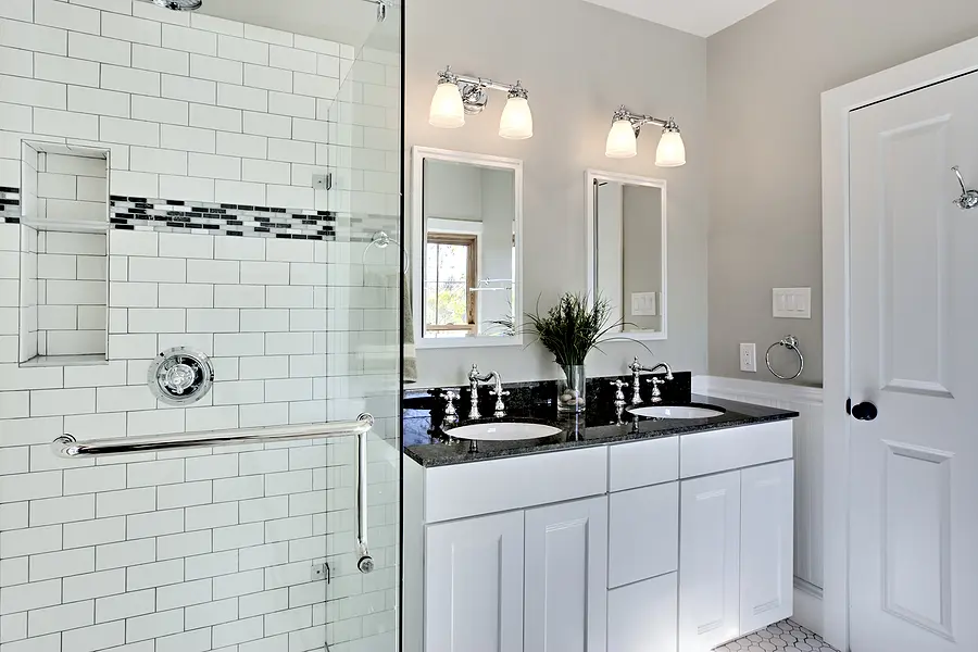 Newly remodeled white bathroom with modern tiled shower and dual sink vanity.